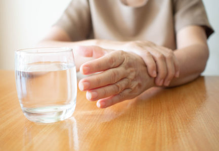 Elderly woman hands w/ tremor symptom reaching out for a glass