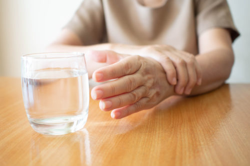 Elderly woman hands w/ tremor symptom reaching out for a glass