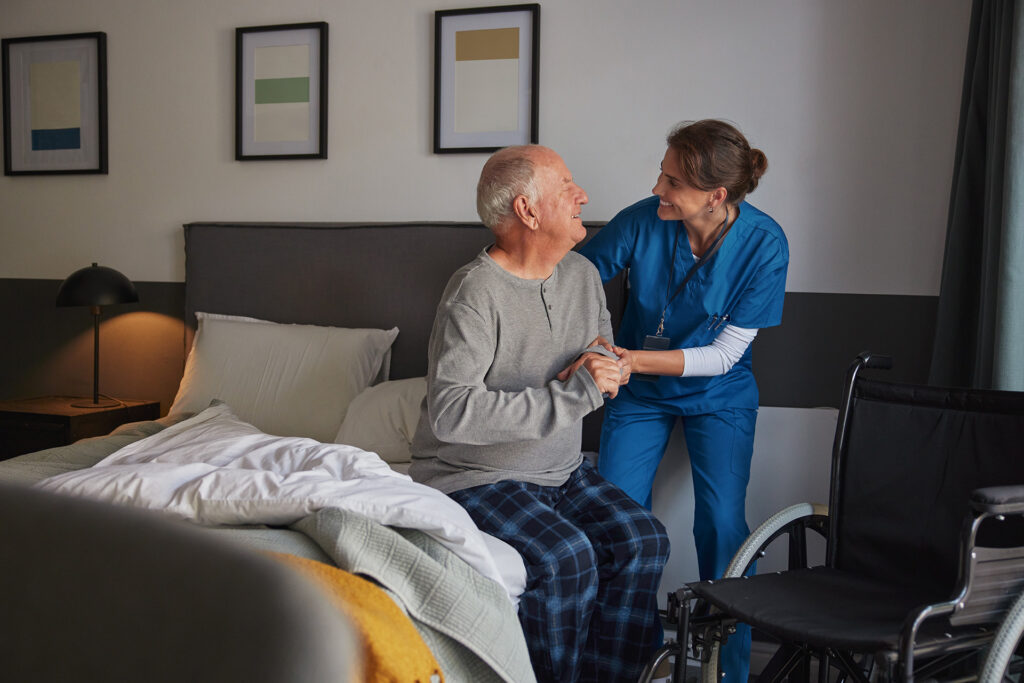 Elderly disabled man getting out of bed with caregiver