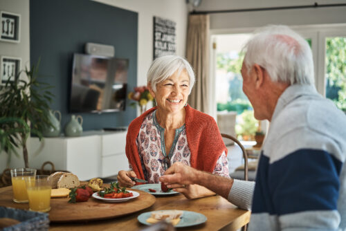Smiling senior woman talking with her husband during a healthy breakfast at their dining table at home in the morning